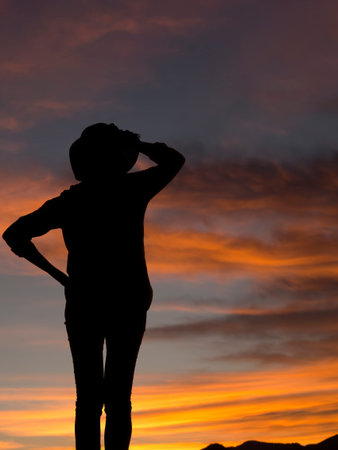 Woman in trousers with hat silhouette looking at sunset, sunrise. Background with copyspace.の写真素材
