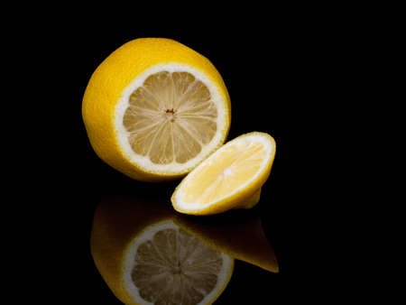 Fresh lemon fruit, sliced, on shiny black reflective background.の写真素材