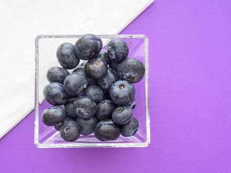 Healthy superfood blueberries in square glass bowl. Purple surface with white napkin for modern, colour block style.の写真素材