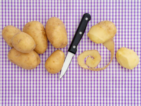 Food preparation, peeling potatoes on purple gingham surface. With knife, overhead view with copyspace. Retro styling.の写真素材