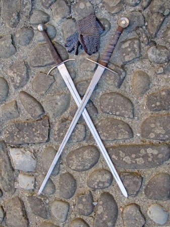 Two medieval swords, crossed, on cobblestones with chain mail gloves.の写真素材