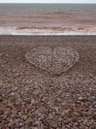 Large love heart shape made with pebbles on beach. Vertical crop.