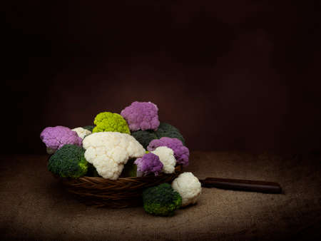 Naturally colourful vegetables in basket, chiaroscuro style dark still life. Assorted raw cauliflower, with broccoli florets. Healthy assortment.の写真素材