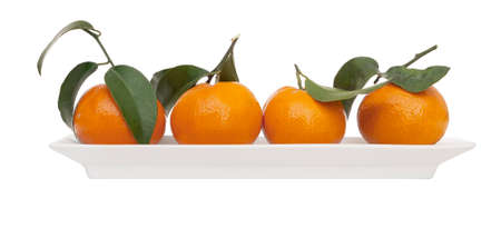 Four juicy small oranges, tangerines, with leaves on white plate isolated on white. Modern, minimalist fresh fruit.の写真素材