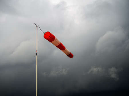 Red windsock on black stormy sky. Bad weather, meterological wind indicator.の写真素材