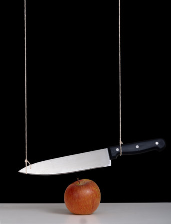 Sword of Damocles threat, risk concept, metaphor - large knife tied and suspended over apple. Still...