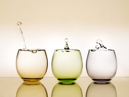Water falls. Drips in three colourful glasses.
