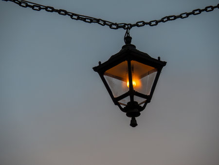 Old style iron street lamp, suspended from chain, alight, in the evening. England.の写真素材