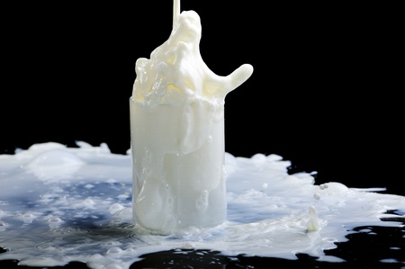 pouring a glass of milk creating splash on black background の写真素材