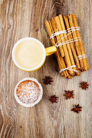 Cup of coffee, a cake and cinnamon sticks on wooden background. Toned imageの写真素材