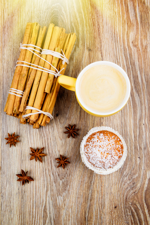 Cup of coffee, a cake and cinnamon sticks on wooden background. Toned imageの写真素材