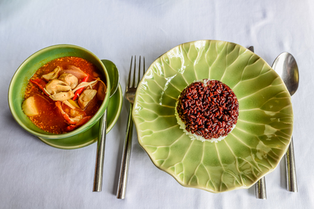 Brown rice and white rice with Thai popular soup, called Tom Yum Kung soup on white fabric platematの写真素材