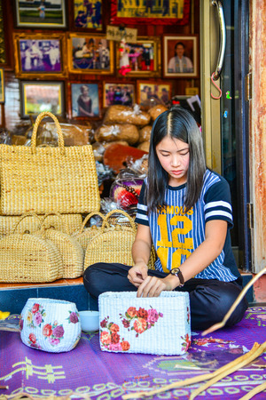 Phayao, Thailand - February 15, 2014: Woman attaching flower sticker to wicker handbag made from papyrus in Phayao, Thailandのeditorial素材