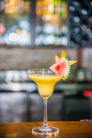 Cocktail drink in yellow favor with piece of watermelon and orange on top on wooden cocktail barの写真素材