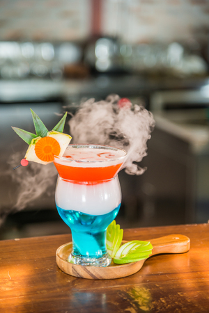 Cocktail drink with smoke decorated with some sliced green apple in wooden plate on wooden cocktail barの写真素材