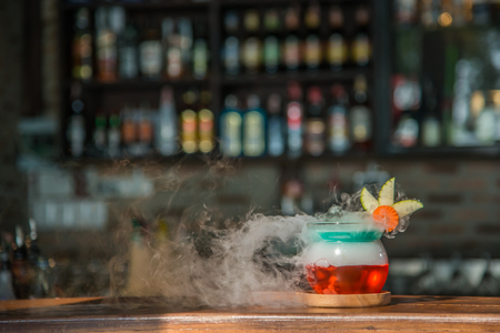 Cocktail drink in red favor with smoke on wooden plate on wooden cocktail barの写真素材