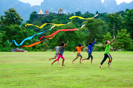 Kanchanaburi, Thailand - September 15, 2011: Group of rural children playing kite together on  field in fron of Buddhist temple on hill in Kanchanaburi, Thailandのeditorial素材