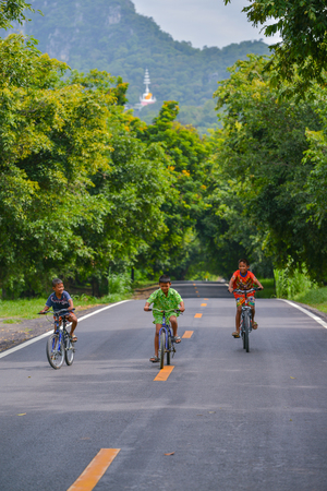 Lopburi, Thailand - July 21, 2013: Three boys with different color shirts riding bicycles on rural road in Lopburi, Thailandのeditorial素材