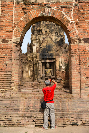 Lopburi, Thailand - July 20, 2013: Red shirt photographer shooting beautiful rock Buddha Image in ruined historical public park in Lopburi, Thailandのeditorial素材