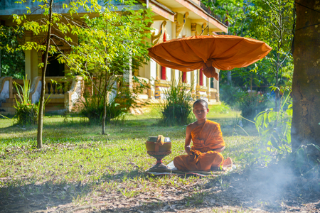 Krabi, Thailand - May 2, 2015: Novice monk meditating on field under long-handled umbrella close to Buddhist church in Krabi, Thailandのeditorial素材