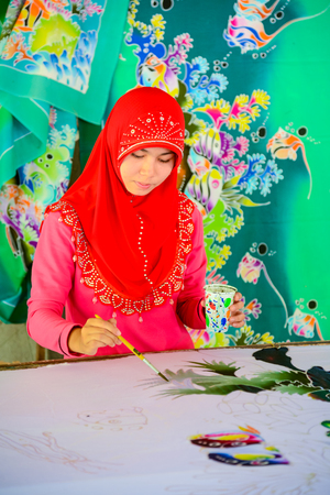 Krabi, Thailand - May 2, 2015: Beautiful Muslim woman wearing red hijab painting pattern on Batik fabric in Krabi, Thailandのeditorial素材
