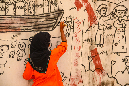 Krabi, Thailand - May 3, 2015: Muslim girl wearing black hijab drawing graphic image on wall of ruined house in Krabi, Thailandのeditorial素材