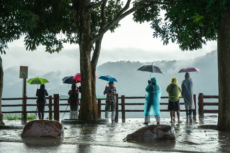 Nakhon Ratchasima, Thailand - September 30, 2018: Tourist photographers holding umbrellas taking landscape view of hills during raining in Khao Yai, national park in Nakhon Ratchasima, Thailandのeditorial素材