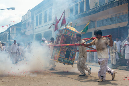 Phang Nga, Thailand - October 14, 2018: Group of men in white dress holding palanquin with Chinese god statue inside  marching on street while people fire firecracker to worship the god in vegetarian festival parade in Phang Nga, Thailandのeditorial素材