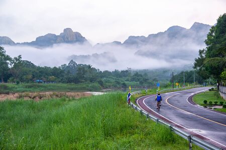Phang Nga, Thailand - October 15, 2018: Blue shirt cyclist's riding bicycle on country road with beautiful scenic in the morning in rural village in Phang Nga, Thailandのeditorial素材