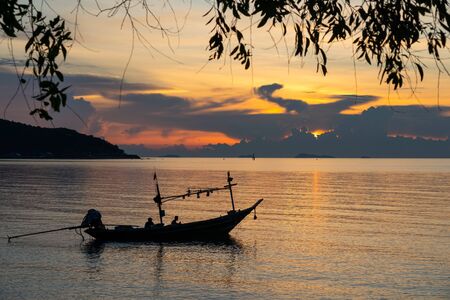 Silhouette fishing boat parking on sea with two unidentified silhouette fishermen during beautiful sunsetの写真素材