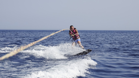 A man wakeboarder clings to a cable and moves behind a boat on the seaの写真素材