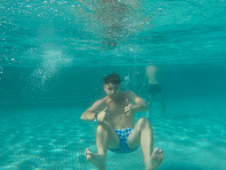 A Man floating under water in the pool with thumbs upの写真素材