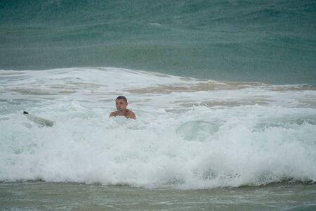 Young man swims on a surfboard in the ocean in the rainの写真素材