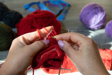 Woman hands knitting sock with needles and yarn of red color. Clews threads of red, lilac and dark...