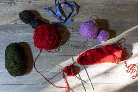 Sock in the process of knitting with needles and yarn of red color on a gray wooden table. Clews...