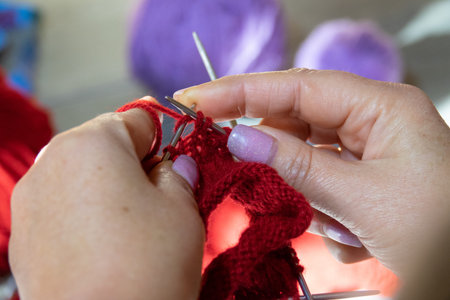 Woman hands knitting sock with needles and yarn of red color. Clews threads of red and lilac color....
