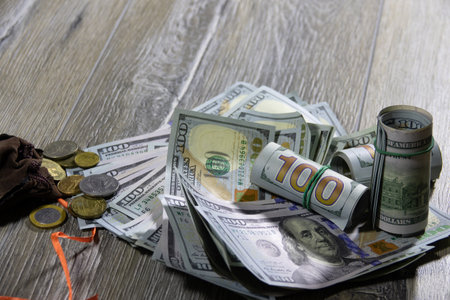 Closeup of one hundred dollar bills of American dollars and a money sack with different coins of the world on a gray wooden table. Banking and financial conceptの写真素材