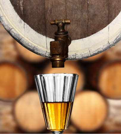 glass underneath a wine or beer wooden keg against wooden barrel backgroundの写真素材