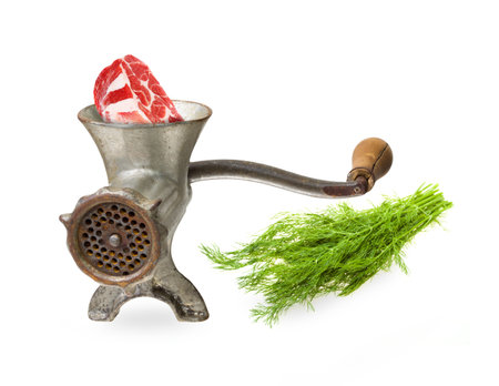 Meat preparation cooking process in manual meat mincer. Selective focus on the meat and mincer front. soft shadows. Bunch of green dill is on background- slightly gradientally blurred. の写真素材