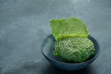 an organic, vitamin-rich and crunchy savoy cabbage in a delicate blue clay bowl on a gray background. perfect for diet-related illustrationsの写真素材