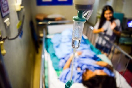 Close up saline IV drip and patient in hospitalの写真素材