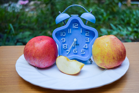 alarm clock and apple on dishの写真素材