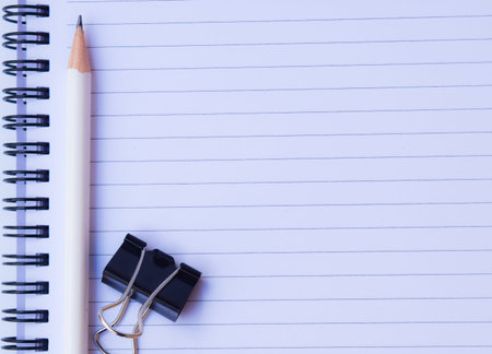 notebook paper with white pencil and black paper clip on white background for texture