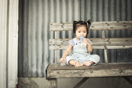 asian baby girl with bottle of milk sitting alone on tableの写真素材
