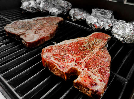 T-bone steak grilled on a hot and smoky oven sprinkled with pepper and salt and dried rosemary with side dishes wrapped in foil and grilled on the stove.の写真素材