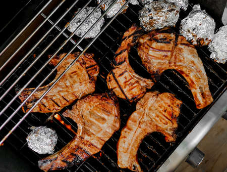 T-bone steak grilled on a hot and smoky oven sprinkled with pepper and salt and dried rosemary with side dishes wrapped in foil and grilled on the stove.の写真素材