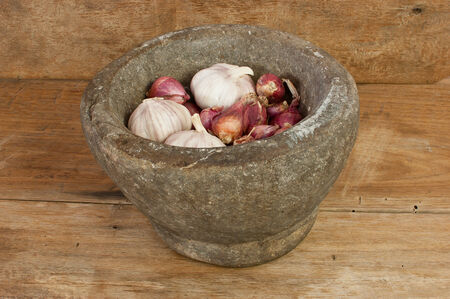 Mortar made of stone with garlic, shallots on a wooden floor.の写真素材