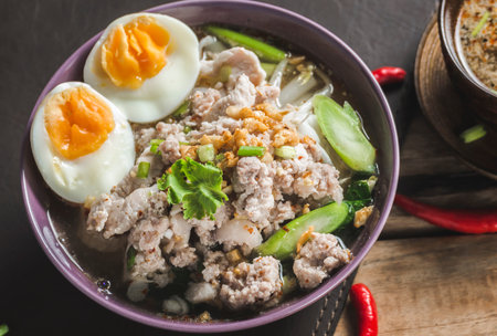 Spicy Tom Yam Wide Rice noodles soup with Vegetables and meats on Wooden Table.の写真素材
