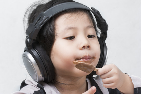Portraits a little Cute asian girl listen to music and eat ice cream happily on white background.の写真素材