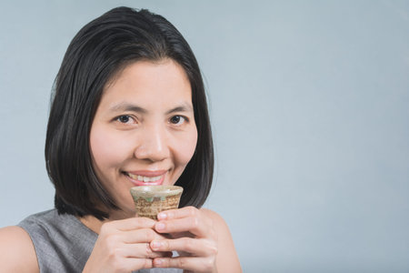 Beautiful Asian woman with a cup of sake in hand. To drink happily on gray Background.の写真素材